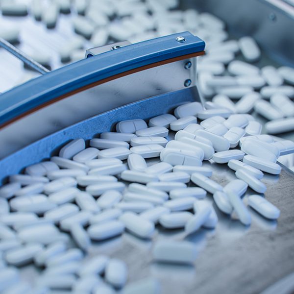 Tablets and Capsules Manufacturing Process. Close-up Shot of Medical Drug Production Line. White Painkiller Pills are Moving on Conveyor at Modern Pharmaceutical Factory.
